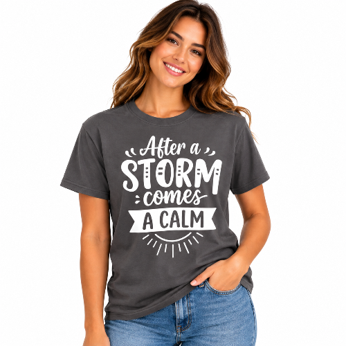 Woman wearing a charcoal gray After a Storm Comes a Calm graphic T-shirt with white lettering.