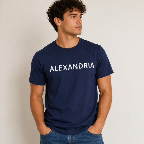 A man wearing a navy blue crewneck t-shirt with the word 'ALEXANDRIA' printed in white across the chest, paired with blue jeans, standing against a plain light gray background.