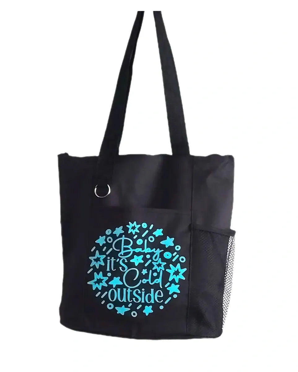 Black tote bag with blue “Baby It’s Cold Outside” text and snowflake star design, reusable fabric shoulder bag on white background
