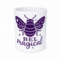 A white ceramic mug featuring a purple graphic of a bee with the text 'BEL magical' printed below it, set against a plain white background.