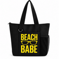 Black reusable tote bag with bold yellow Beach Babe text and sunglasses graphic, long shoulder straps, zipper closure, silver D-ring, front pocket, and side mesh pocket.