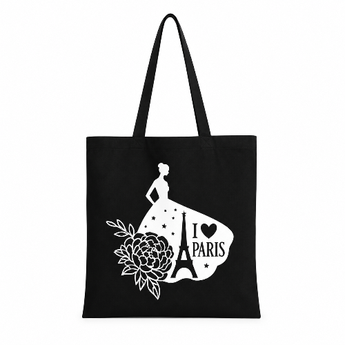 A black canvas tote bag with long black handles, featuring a white graphic print of a woman in a dress, the Eiffel Tower, a flower, and the text 'I <heart> PARIS'.