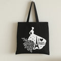 Black cotton tote bag with white Paris graphic, Eiffel Tower silhouette, and floral artwork, reusable travel shopper tote for shopping, school, vacation, books, errands, and everyday fashion use
