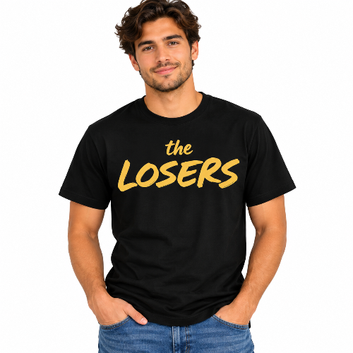 Man wearing a black The Losers graphic T-shirt with bold mustard yellow lettering.