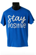 Blue graphic t shirt featuring the phrase Stay Positive in white script lettering on a bright blue unisex short sleeve tee designed for everyday casual wear.