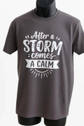 Charcoal gray graphic t shirt featuring the inspirational quote After the Storm Comes a Calm in a vintage typography design promoting hope, strength, and resilience.