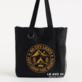 Black tote bag featuring a city and mountain emblem design in gold tones. Reusable shoulder tote bag for shopping, work, school, travel, books, groceries, and everyday errands. Lightweight and durable carryall with comfortable straps and an outdoor-inspired graphic. Perfect for travelers, hikers, campers, outdoor enthusiasts, and lovers of modern adventure-themed accessories.