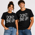 Male and female models wearing matching black unisex “Don’t Give Up!” graphic T-shirts with bold white lettering.