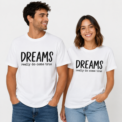 A man and a woman modeling matching white graphic t-shirts with the black printed text 'DREAMS really do come true' on the chest, paired with blue jeans against a clean white background.
