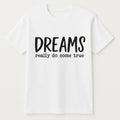 White graphic t-shirt featuring the inspirational phrase "Dreams Really Do Come True" in bold black typography. Motivational unisex shirt designed for positivity, encouragement, goal setting, personal growth, and everyday casual wear.