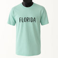 Mint green graphic t-shirt featuring the word "Florida" in bold black typography. Casual unisex travel-inspired shirt perfect for beach vacations, Florida lovers, tourists, road trips, summer outfits, and everyday wear.