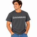 A man wearing a dark charcoal gray t-shirt with the word 'SAVANNAH' printed in white across the chest, paired with blue jeans, set against a plain white background.
