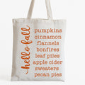 White reusable Hello Fall Autumn tote bag with orange seasonal word list design featuring pumpkins, cinnamon, bonfires, apple cider, sweaters, and pecan pies. Lightweight tote perfect for shopping, farmers markets, fall festivals, errands, and cozy autumn everyday use.