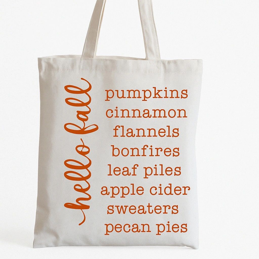 White reusable Hello Fall Autumn tote bag with orange seasonal word list design featuring pumpkins, cinnamon, bonfires, apple cider, sweaters, and pecan pies. Lightweight tote perfect for shopping, farmers markets, fall festivals, errands, and cozy autumn everyday use.