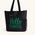 Black tote bag featuring the phrase "Hello Winter" in bold green lettering. Reusable winter-themed tote perfect for shopping, errands, holiday outings, work, travel, books, groceries, and everyday essentials. Lightweight and durable shoulder bag designed for winter lovers, seasonal gifting, and cozy cold-weather style.