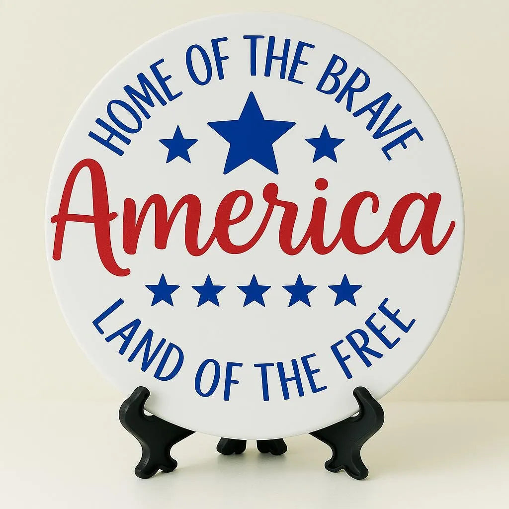 Patriotic America coaster with red white and blue lettering, stars, and “Home of the Brave Land of the Free” design, decorative tabletop coaster for patriotic home decor, 4th of July decorations, Memorial Day gifts, Veterans Day table accents, Americana shelf decor, farmhouse patriotic coaster, festive holiday drink coaster for coffee table and office desk styling.