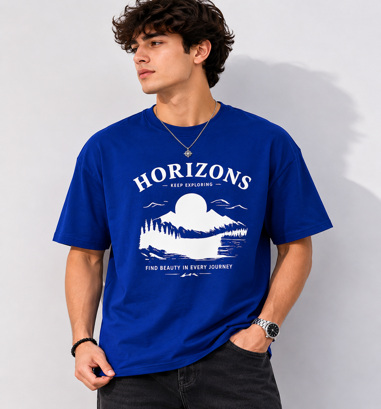 Male model wearing oversized royal blue Horizon graphic t-shirt with white front print styled with black jeans in modern casual streetwear fashion