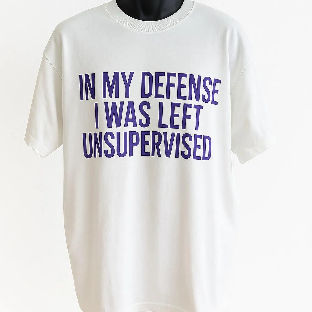 White graphic t-shirt featuring the humorous phrase "In My Defense I Was Left Unsupervised" in bold blue typography, funny unisex graphic tee.