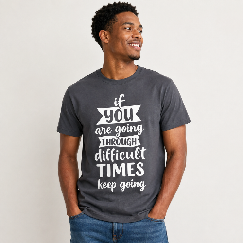 A man wearing a dark gray graphic t-shirt with the white printed text 'if you are going THROUGH difficult TIMES keep going', paired with blue jeans, against a plain light gray background.
