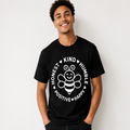 A smiling man wearing a black crewneck t-shirt with a white graphic of a cartoon bee and the words 'HONEST KIND HUMBLE POSITIVE HAPPY' printed on the front, set against a plain light gray background.