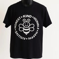 Black graphic t-shirt featuring a white bee illustration surrounded by positive words including kind, honest, humble, happy, resilient, and positive. Inspirational unisex tee promoting kindness, encouragement, positivity, mindfulness, and everyday motivation.
