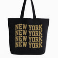 Black cotton tote bag with bold New York typography design in gold lettering, reusable shoulder tote for shopping, travel, city life, work, school, everyday carry, and urban fashion accessories