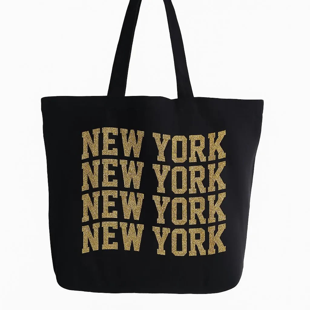 Black cotton tote bag with bold New York typography design in gold lettering, reusable shoulder tote for shopping, travel, city life, work, school, everyday carry, and urban fashion accessories