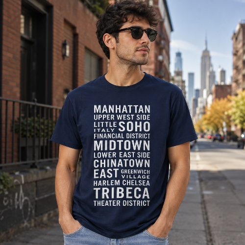 A man wearing a navy blue graphic t-shirt with white text listing various Manhattan neighborhoods, standing on a city sidewalk with a blurred urban background.