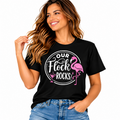 Our Flock Rocks black graphic T-shirt with pink flamingo design styled with blue jeans.