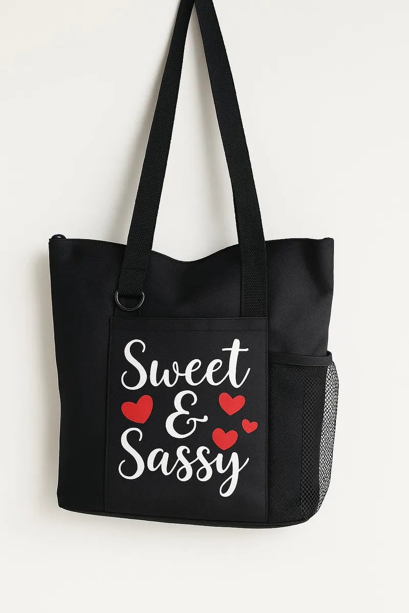 Black tote bag featuring a Sweet & Sassy quote design with decorative hearts. Reusable shoulder tote bag for shopping, work, school, travel, books, groceries, and everyday errands. Lightweight and durable carryall with comfortable straps and a fun, stylish design. Perfect gift for women, teens, friends, daughters, and anyone with a confident personality.