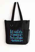 Black tote bag featuring the phrase "Winter Kisses and Snowflake Wishes" in blue winter-themed typography. Reusable seasonal tote perfect for shopping, holiday outings, work, travel, books, groceries, and everyday essentials. Lightweight and durable shoulder bag designed for winter lovers and festive cold-weather style.